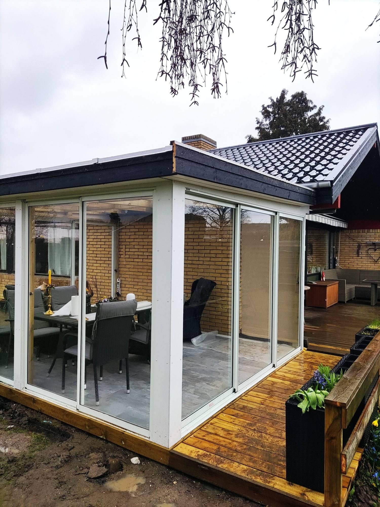 Udestue med glaspartier, sort tag og træterrasse udført af Baaring Entreprise.